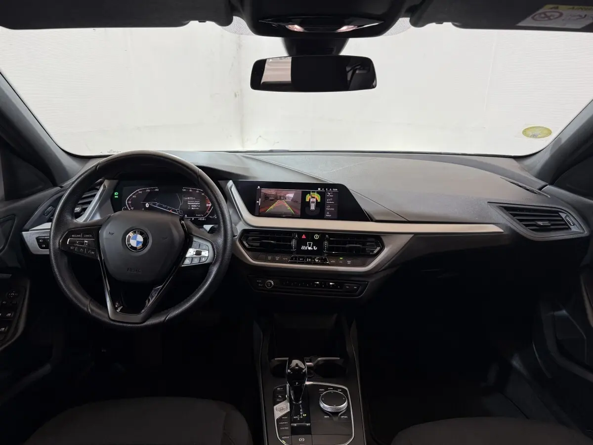Vue intérieure avant de la BMW Série 1 116d Business Design noire, tableau de bord moderne avec écran tactile et volant cuir multifonctions.