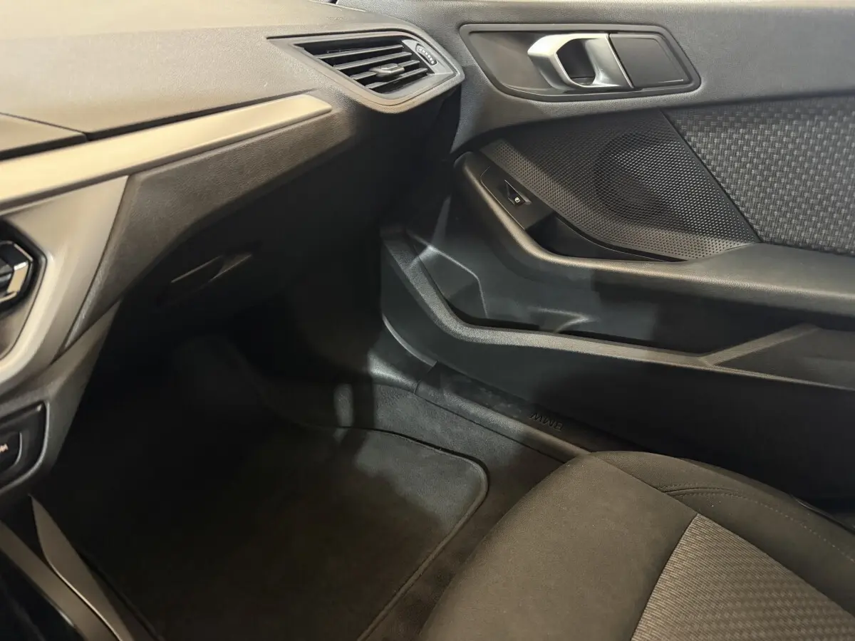 Vue intérieure côté passager avant de la BMW Série 1 116d noire, montrant la portière et le tableau de bord.