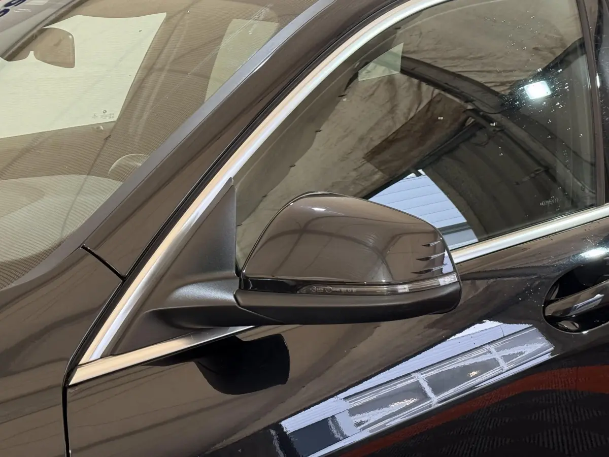 Gros plan sur le rétroviseur côté gauche d’une BMW Série 1 noire, avec poignée de porte et contours chromés visibles.