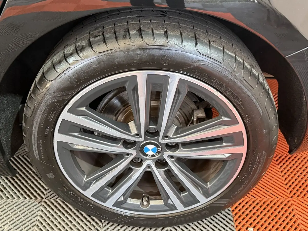 Gros plan sur la roue avant droite d'une BMW Série 1 noire avec jante alliage à dix branches.