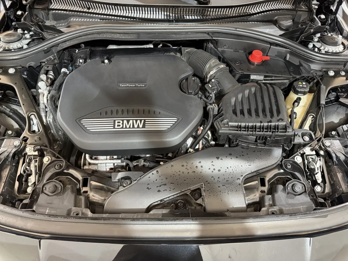 Vue plongeante sur le moteur TwinPower Turbo d'une BMW Série 1 116d noire, avec capot ouvert et détails mécaniques visibles.