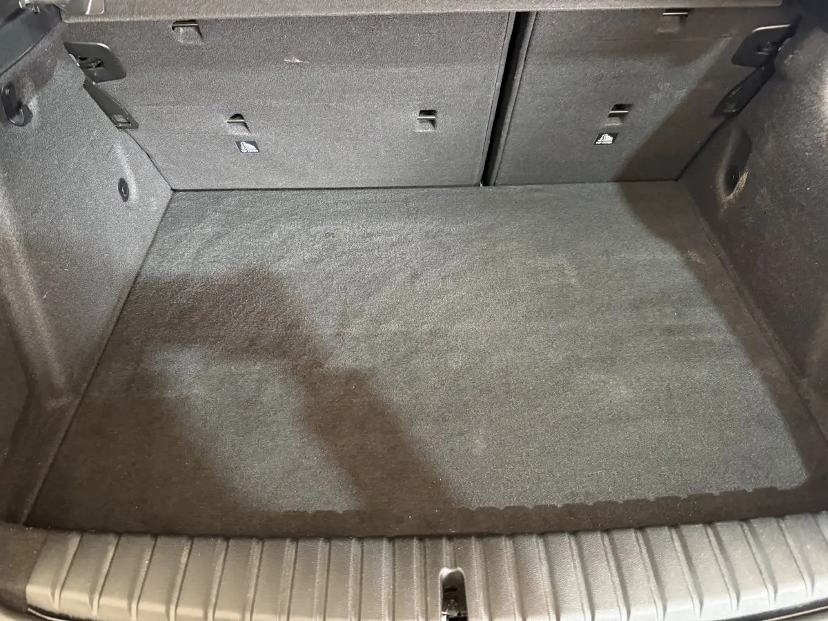 Vue intérieure du coffre noir d'une BMW Série 1 116d DKG7 Business Design, montrant l'espace de chargement avec banquette rabattable.