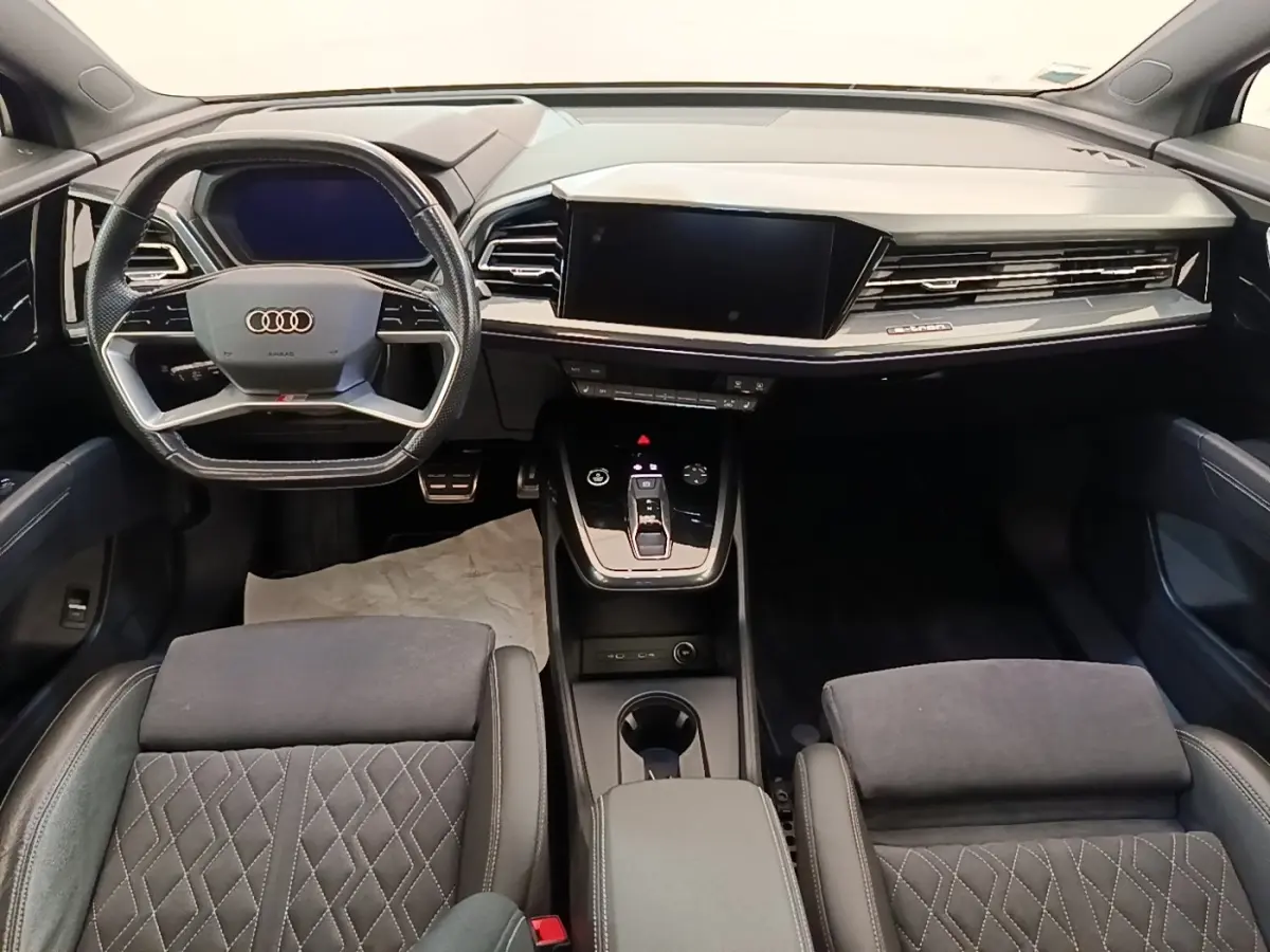Vue intérieure avant de l'Audi Q4 E-TRON Sportback 2023, tableau de bord noir avec écran tactile et volant multifonctions.