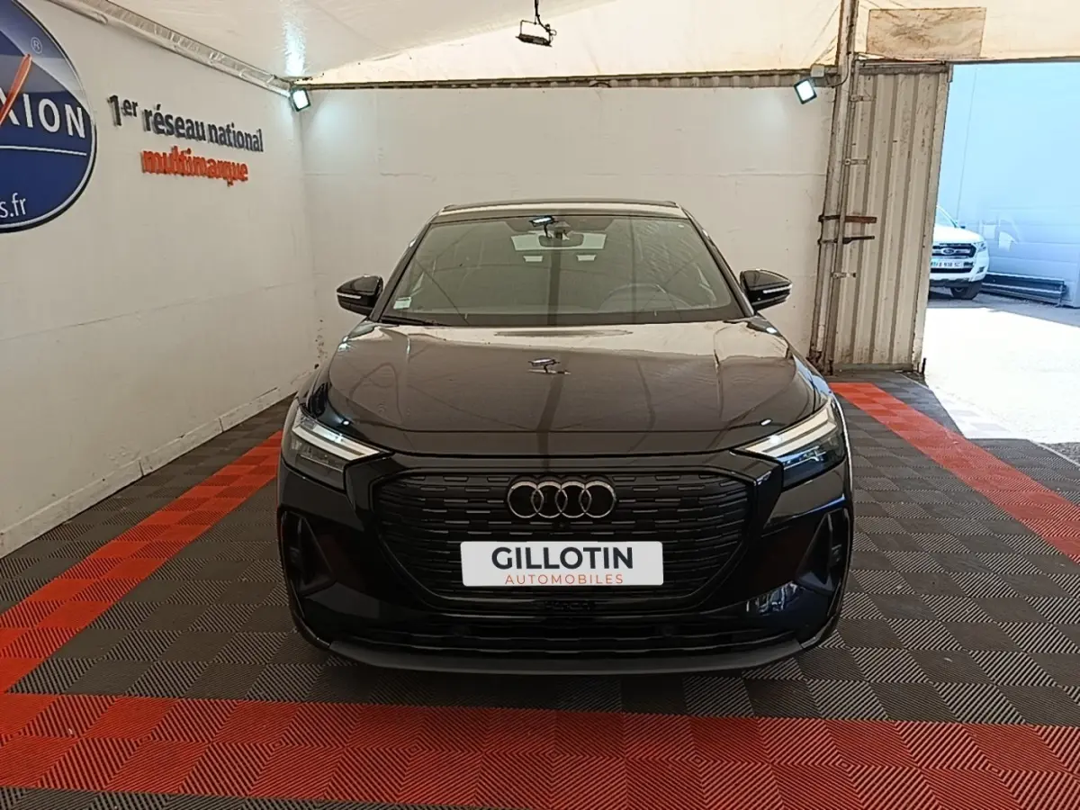 Vue avant d'un Audi Q4 E-Tron Sportback noir, avec calandre noire et phares LED dans un showroom.