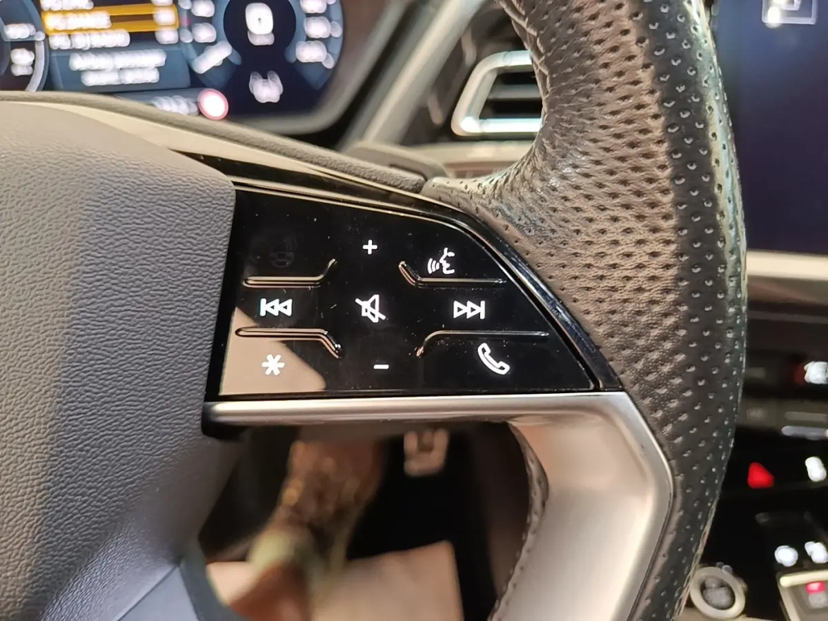 Gros plan sur le volant cuir perforé de l'Audi Q4 E-TRON Sportback, avec commandes tactiles noires et affichage numérique en arrière-plan.