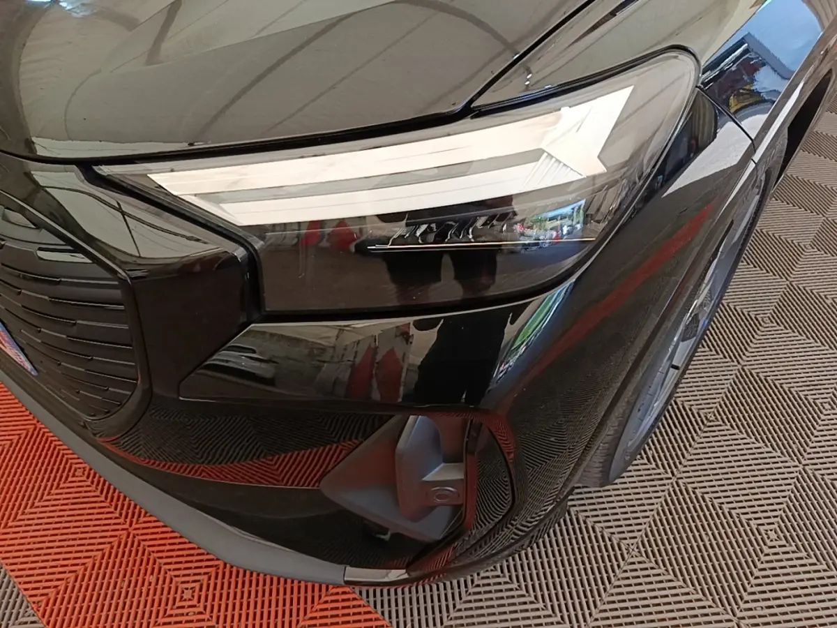 Gros plan sur le phare avant droit noir brillant de l’Audi Q4 E-Tron Sportback 2023 avec calandre et capot visibles.