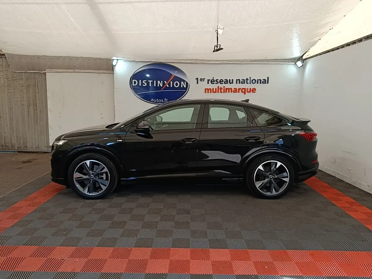 Audi Q4 E-Tron Sportback électrique noir, vue de profil côté gauche en intérieur avec jantes distinctives S Line.
