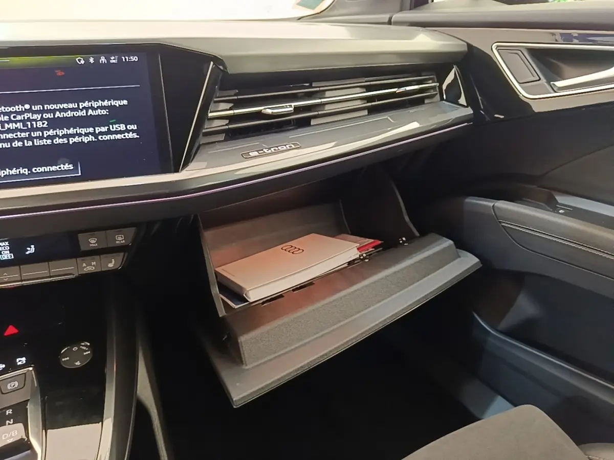 Intérieur noir de l'Audi Q4 E-Tron Sportback 2023, vue sur la boîte à gants ouverte avec documents et écran tactile central.