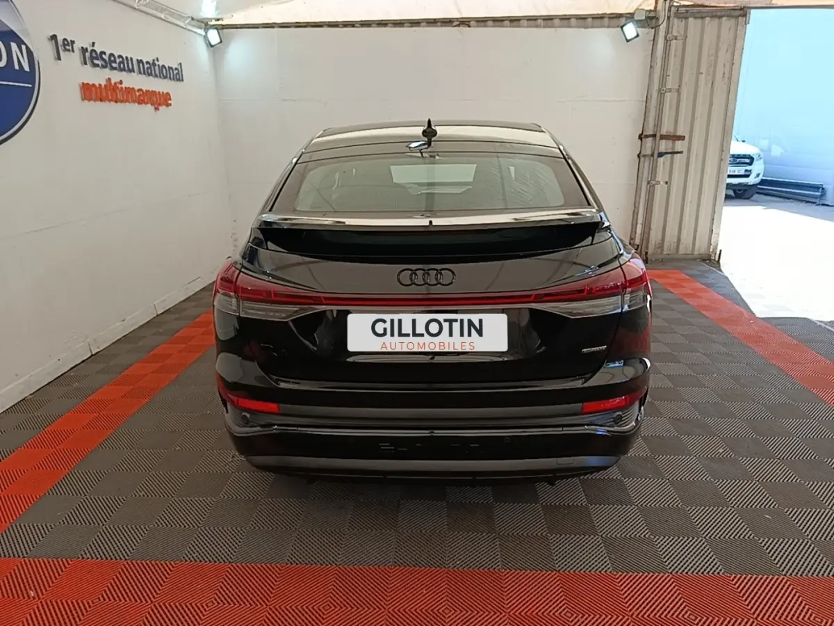 Vue arrière de l'Audi Q4 E-TRON Sportback noir, avec feux LED reliés et spoiler de toit, en intérieur showroom.