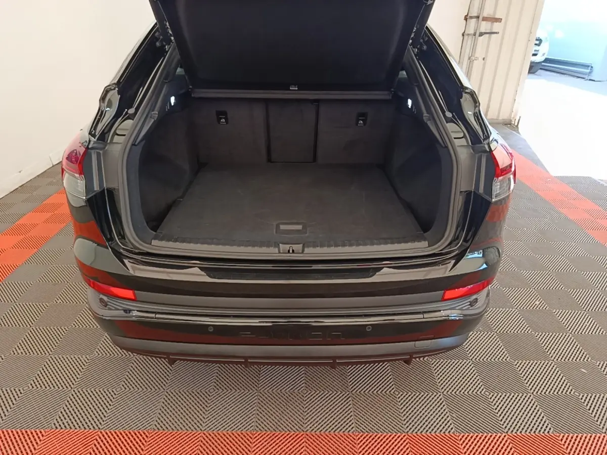 Coffre ouvert vu de l'arrière d'un Audi Q4 E-TRON Sportback noir, montrant l'espace de chargement vide et les feux arrière.