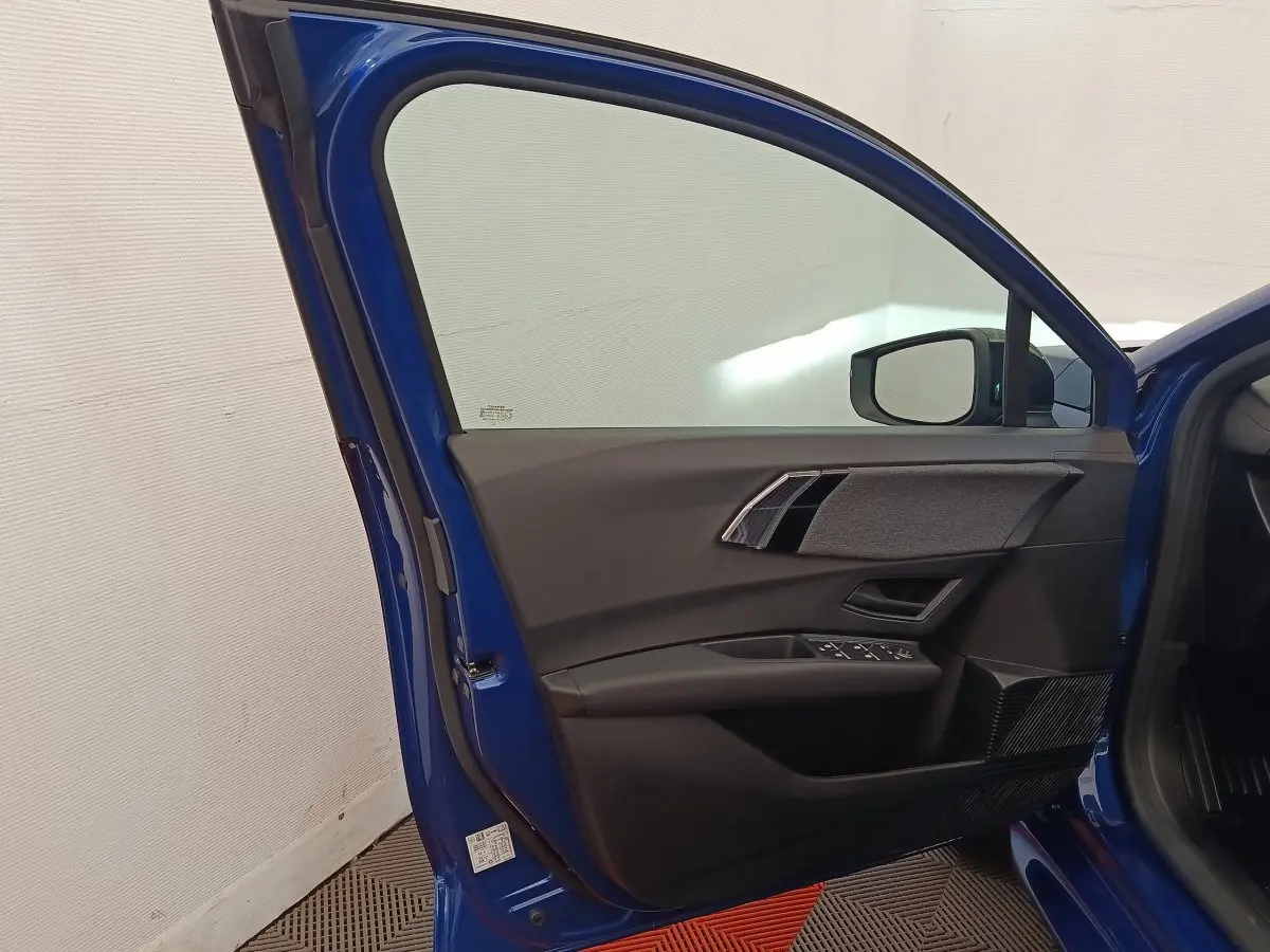 Portière avant gauche ouverte d'une Renault Clio bleu 2026, montrant les commandes de vitre et le rétroviseur intérieur.