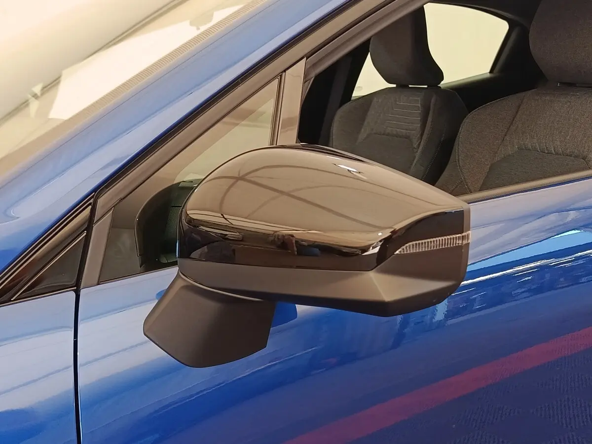 Gros plan sur le rétroviseur droit noir brillant d’une Renault Clio bleu intense, avec intérieur tissu visible.