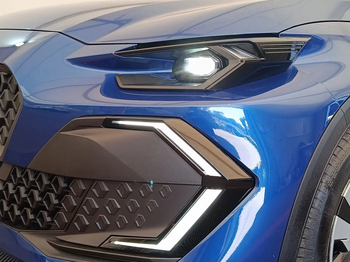 Gros plan sur le phare avant droit allumé de la Renault Clio Evolution TCe 115 bleu brillant avec signature lumineuse en forme de flèche.