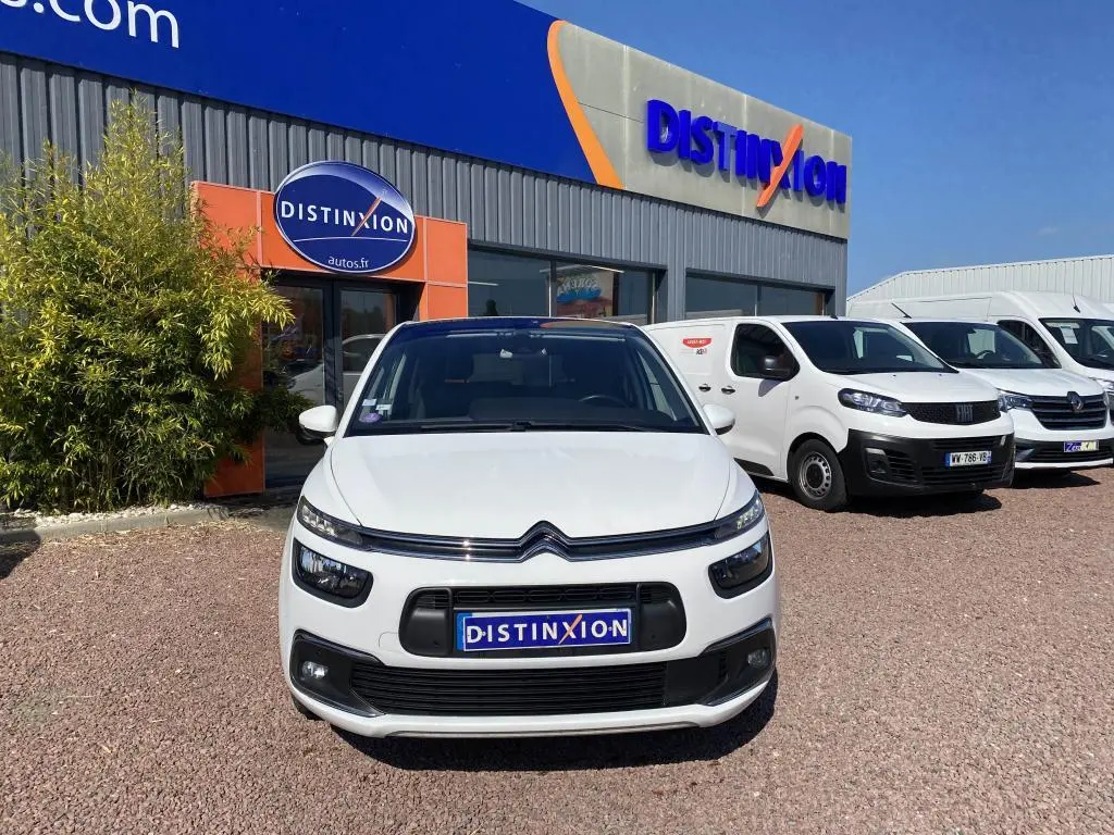 Vue de face d'une Citroën C4 Spacetourer blanche garée devant un concessionnaire Distinxion par temps ensoleillé.