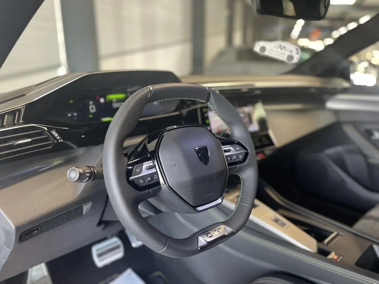 Vue intérieure centrée sur le volant cuir noir GT de la Peugeot 308 2025 avec tableau de bord numérique.