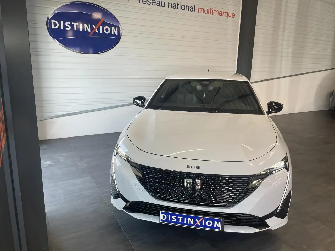 Peugeot 308 blanche vue de face, avec calandre noire brillante et feux LED distinctifs en intérieur showroom.