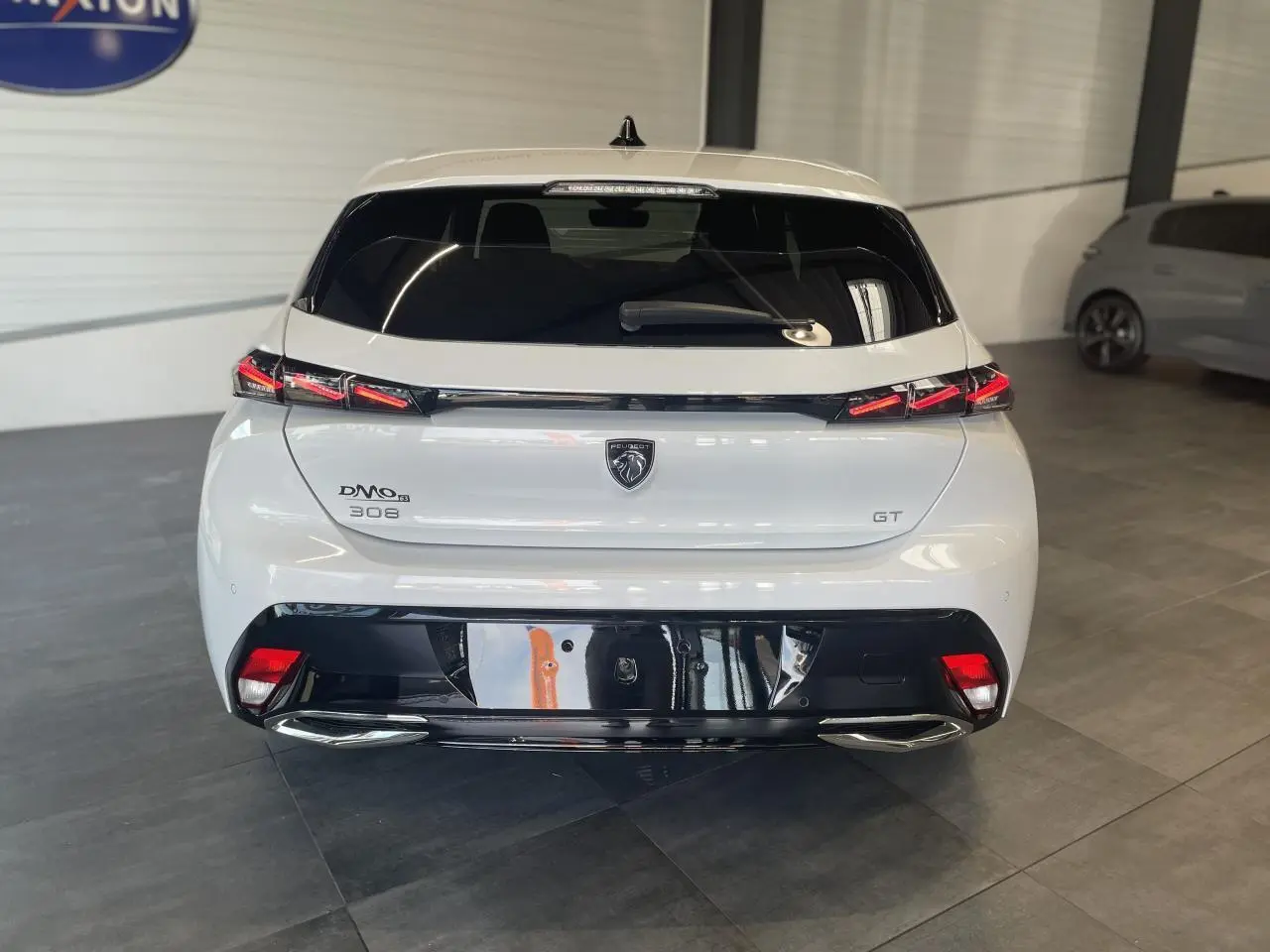 Vue arrière d'une Peugeot 308 GT blanche avec feux arrière à signature lumineuse griffe à griffe et diffuseur noir brillant.