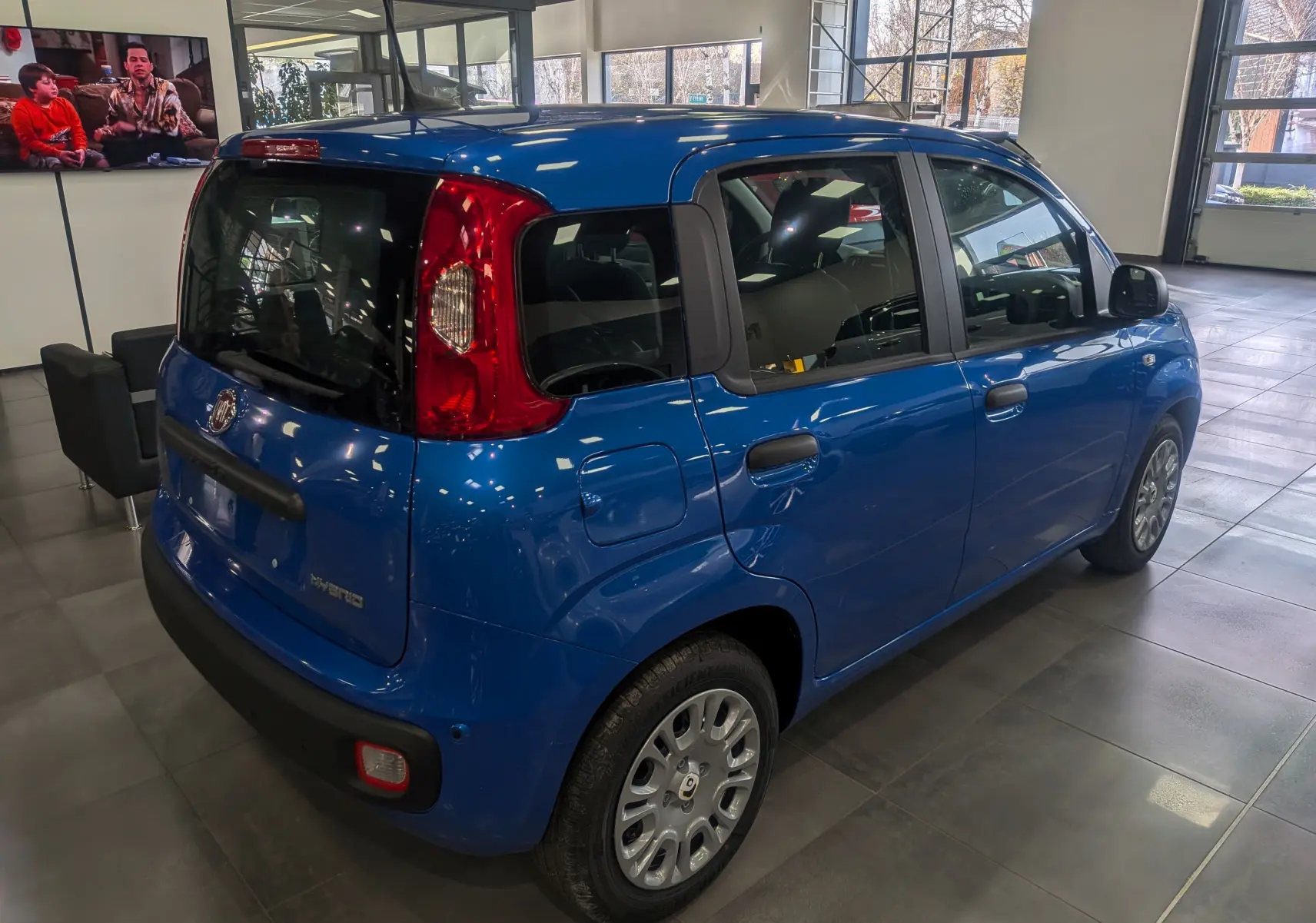 Vue 3/4 arrière droite d'une Fiat Panda 1.0 Hybrid City bleu Italia dans un showroom lumineux.