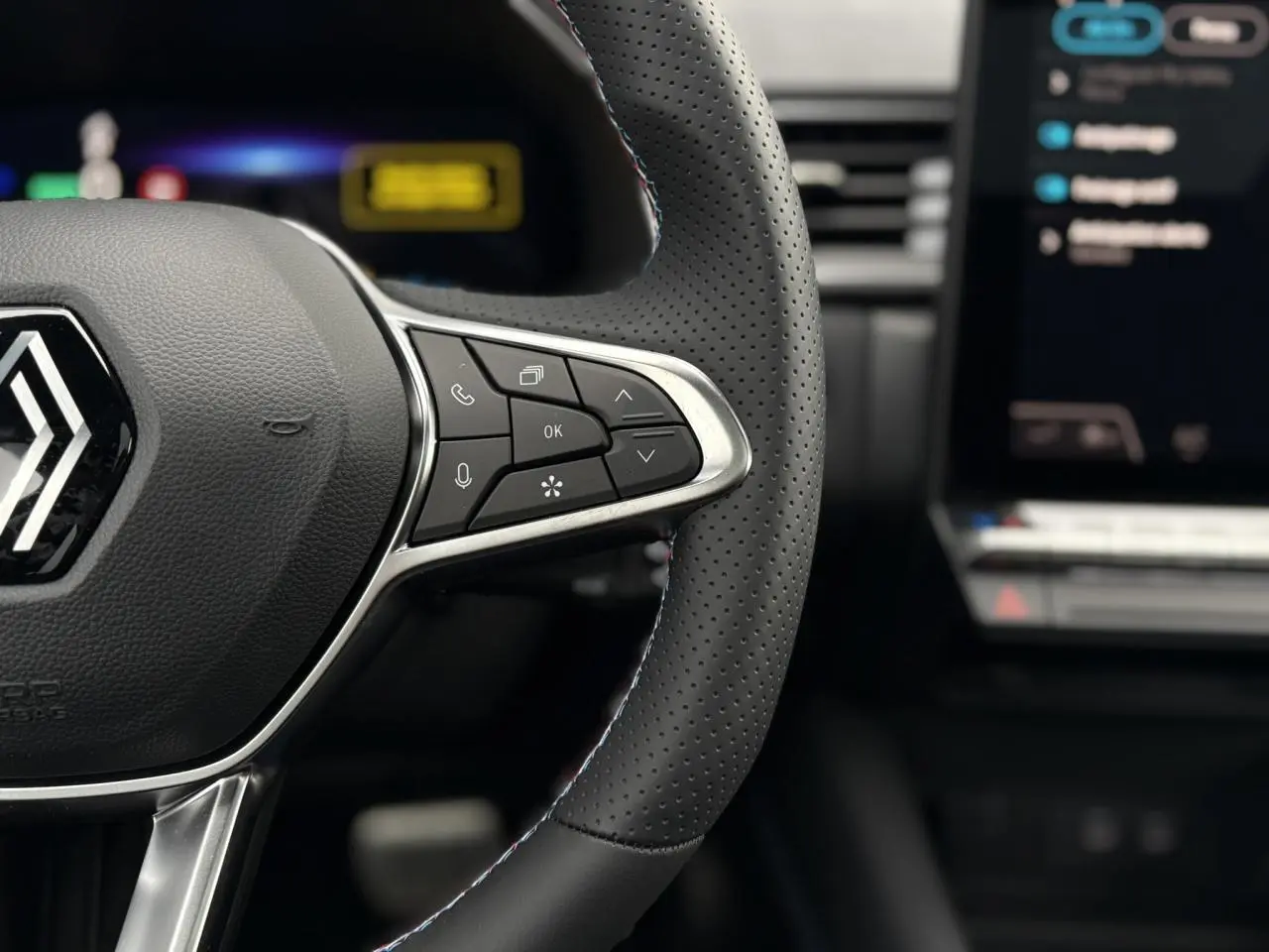 Gros plan sur le volant perforé noir avec commandes multifonctions et logo Renault du Captur E-Tech Full Hybrid 2025.