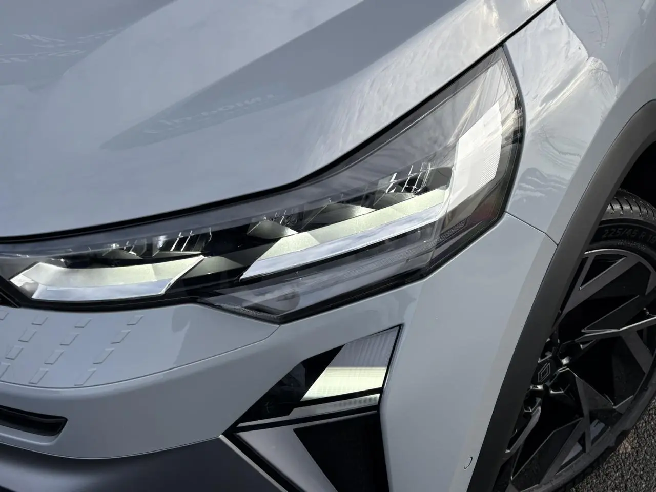 Gros plan sur le phare avant droit du Renault Captur gris Rafale avec jante noire et détails anguleux modernes.