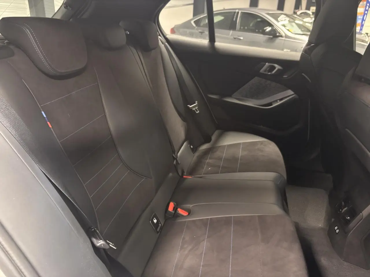 Vue intérieure côté droit des sièges arrière en Alcantara noir avec surpiqûres bleues d'une BMW Série 1 118d M Sport 2025.