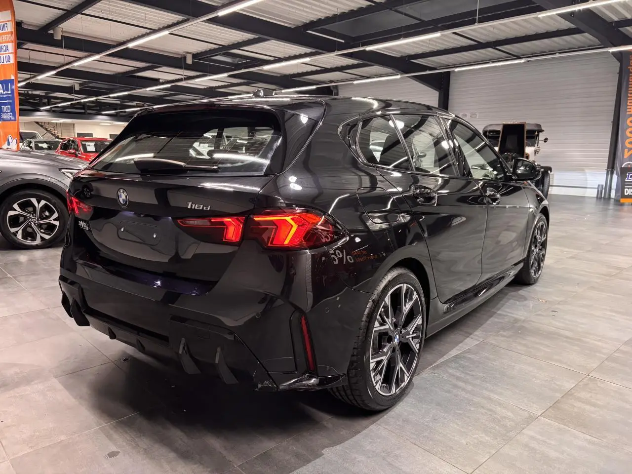 BMW Série 1 118d noire métal vue 3/4 arrière droit en intérieur avec jantes alliage 18 pouces M Sport.