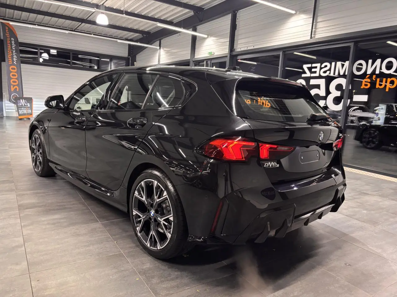 BMW Série 1 118d M Sport noir métal vue 3/4 arrière droit en intérieur avec jantes 18 pouces bicolores et feux LED.