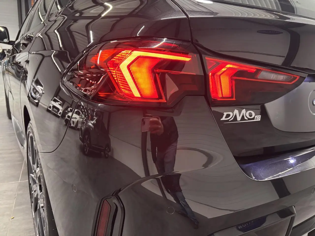 Vue arrière côté gauche d'une BMW Série 1 118d M Sport noire métal avec feux arrière LED allumés.