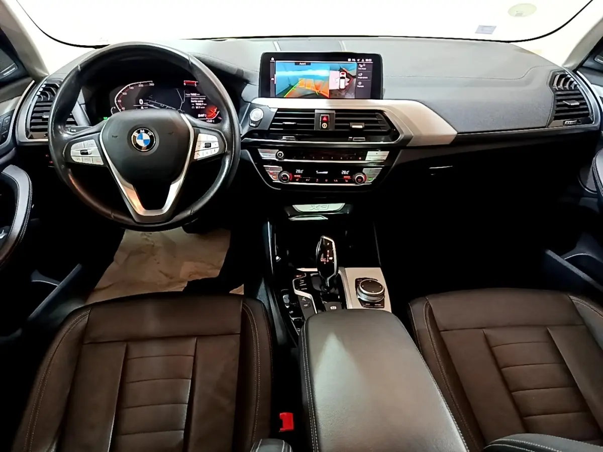 Vue intérieure avant du BMW X3 2019 noir, tableau de bord avec écran tactile et volant cuir multifonctions.