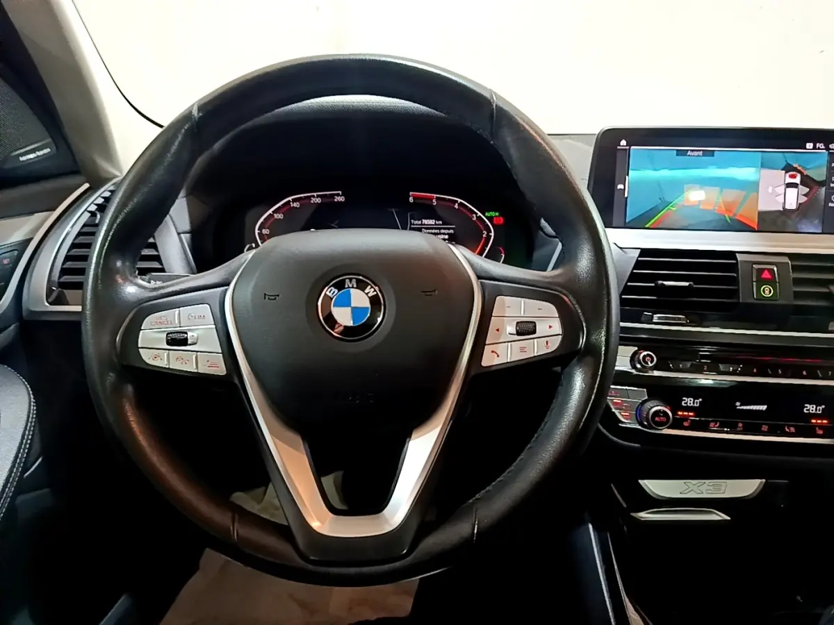 Vue intérieure centrée sur le volant cuir noir et le tableau de bord digital du BMW X3 sDrive18d 2019.