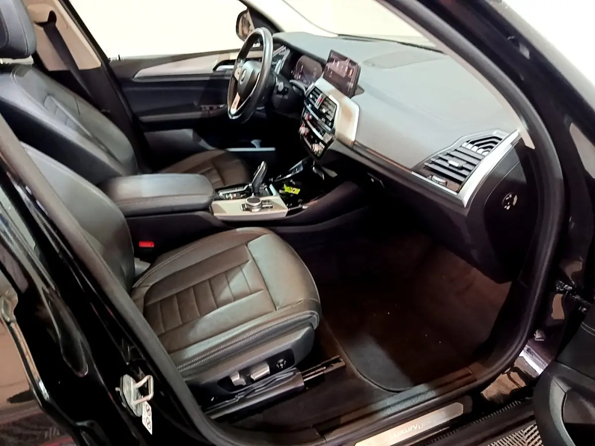 Vue intérieure côté conducteur du BMW X3 noir 2019, montrant sièges cuir et tableau de bord avec écran tactile.