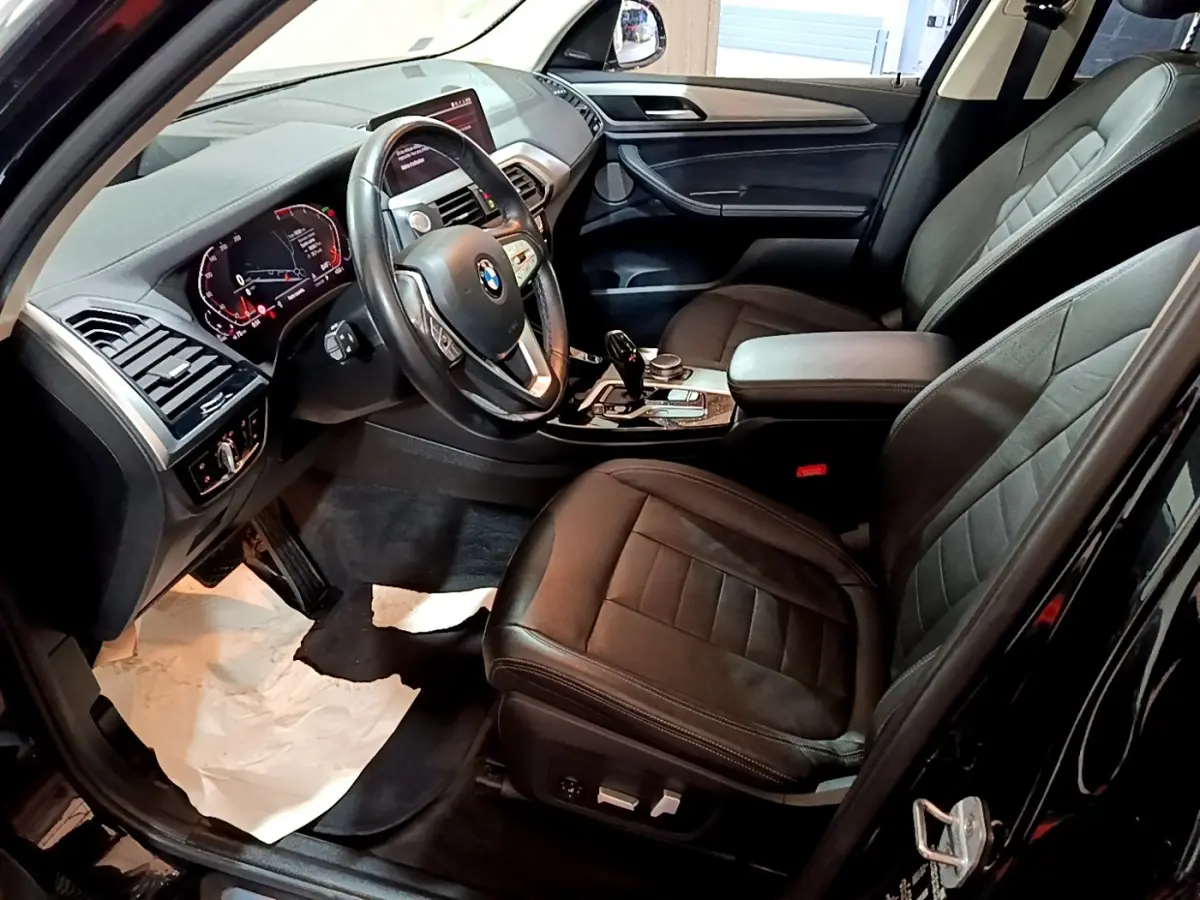 Vue intérieure côté conducteur du BMW X3 noir 2019, avec tableau de bord digital et sièges cuir noirs.