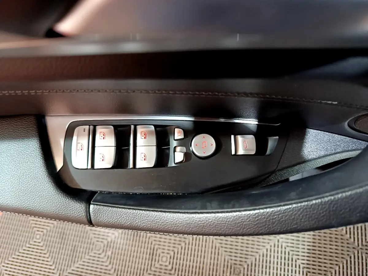 Gros plan sur les commandes des lève-vitres et rétroviseurs côté conducteur d’une BMW X3 noir 2019.