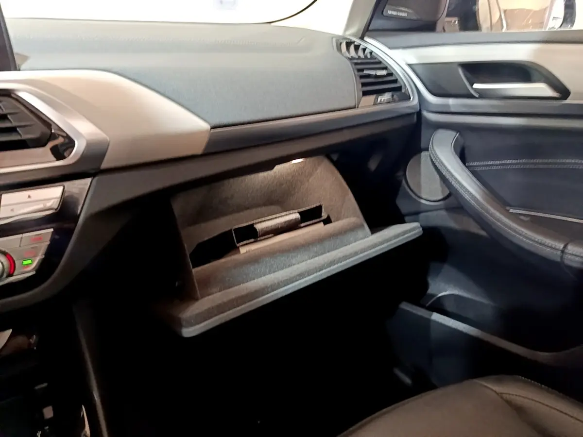 Intérieur BMW X3 sDrive18d 2019, vue côté passager sur boîte à gants ouverte et tableau de bord noir et beige.