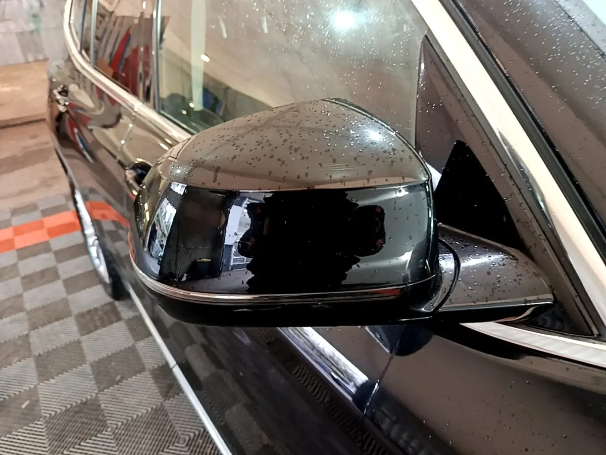 Rétroviseur côté gauche noir brillant avec gouttes d'eau sur BMW X3 sDrive18d Luxury 2019, vue rapprochée en angle.