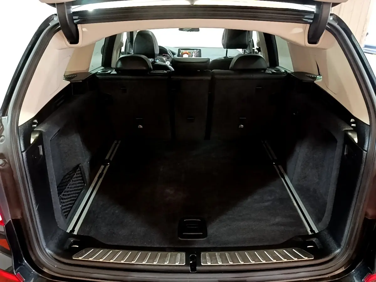Coffre ouvert vu de l'arrière d'un BMW X3 noir, montrant un espace de chargement spacieux et tapis noir.