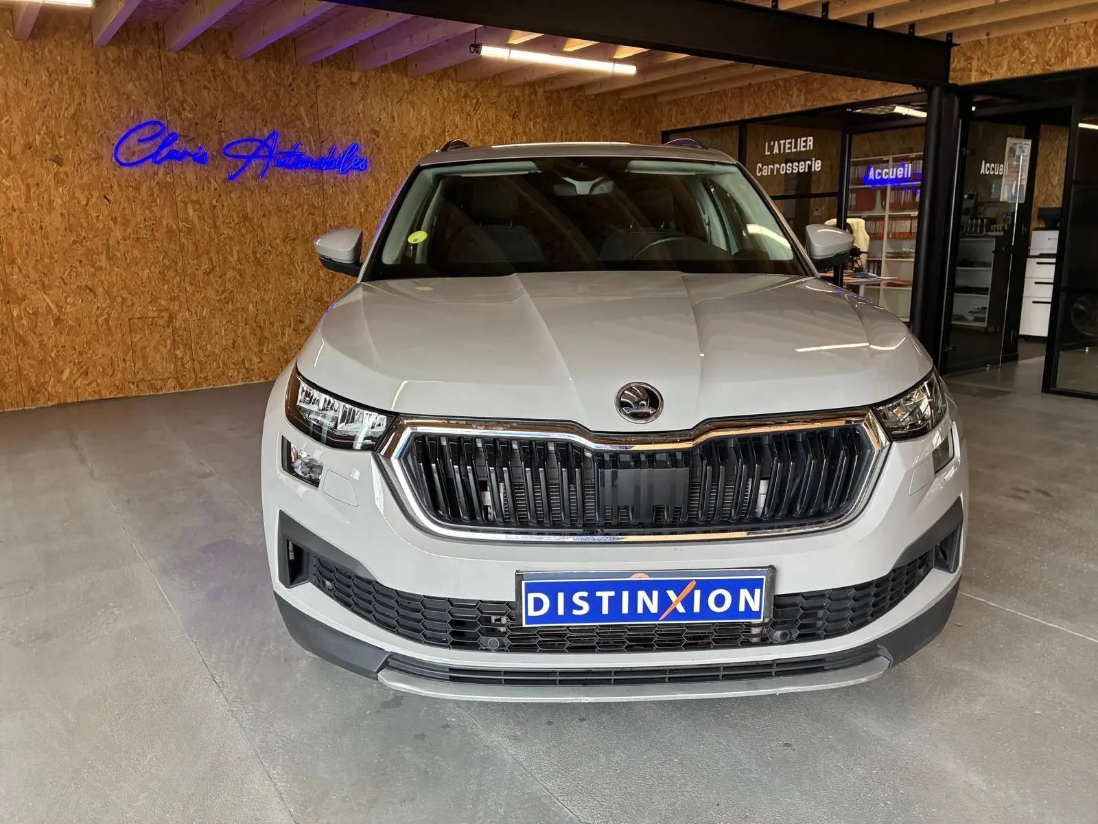 Vue frontale d'un Skoda Kodiaq gris clair 2023 en showroom, avec calandre noire et logo distinctif au centre.