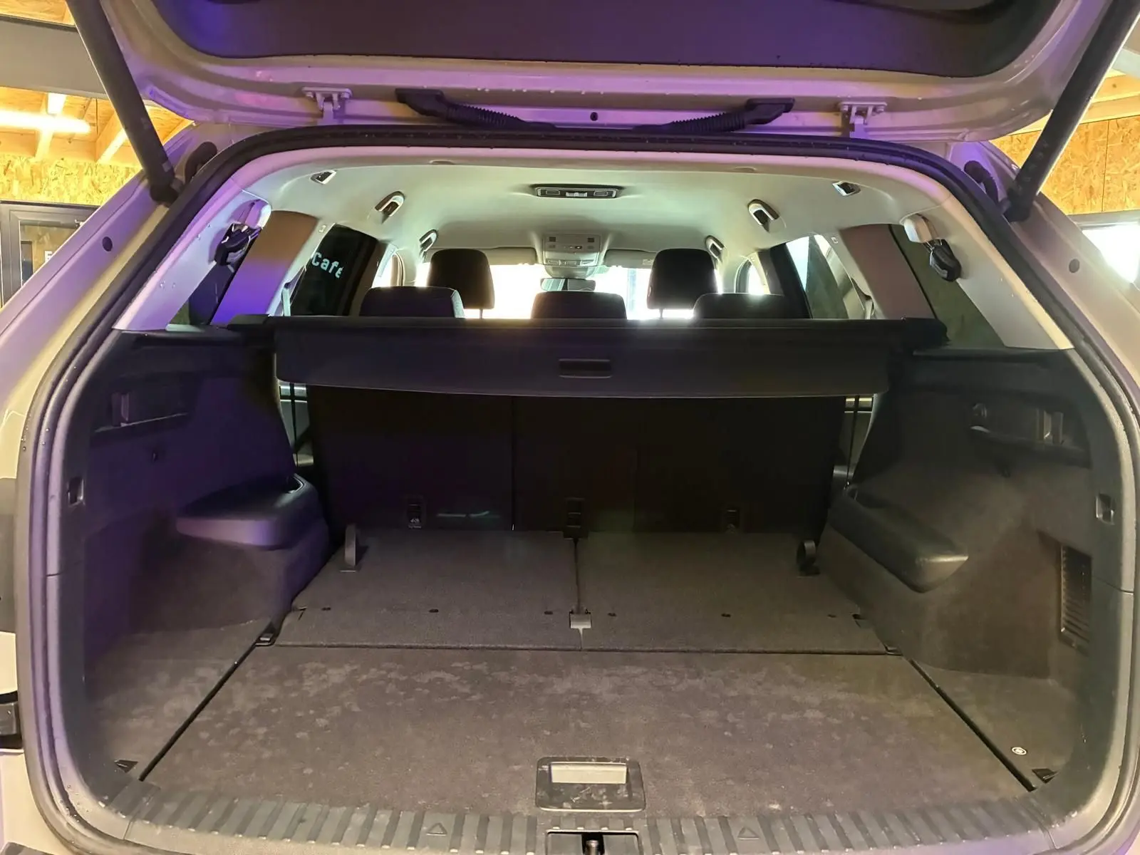Coffre ouvert vu de l'arrière d'un Skoda Kodiaq gris clair 2023, montrant l'espace de chargement et la banquette arrière noire.