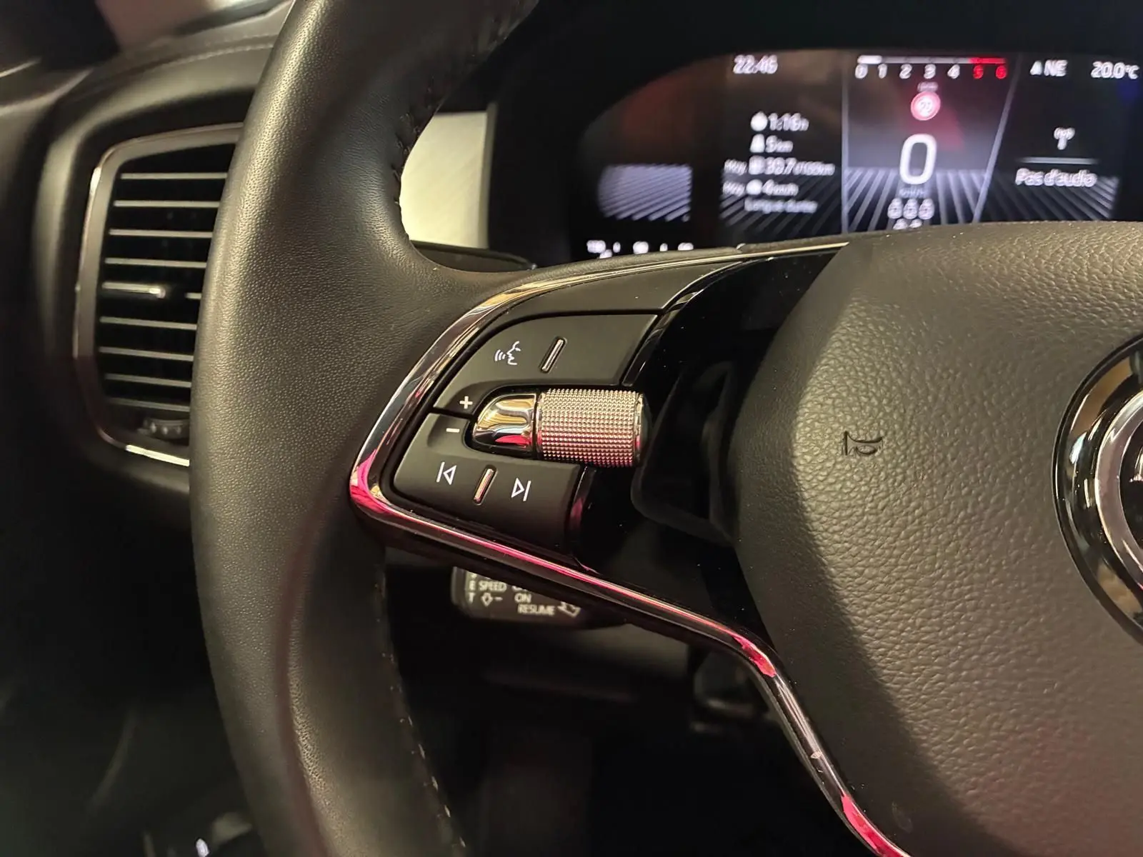 Gros plan sur la partie gauche du volant noir du Skoda Kodiaq gris clair 2023, avec commandes audio et tableau de bord numérique en arrière-plan.