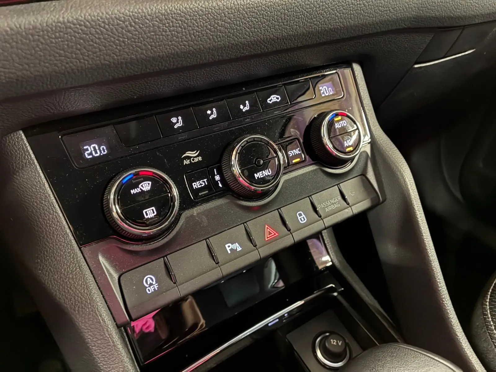 Vue rapprochée du tableau de bord central du Skoda Kodiaq gris clair 2023, mettant en valeur les commandes de climatisation et les boutons de sécurité.