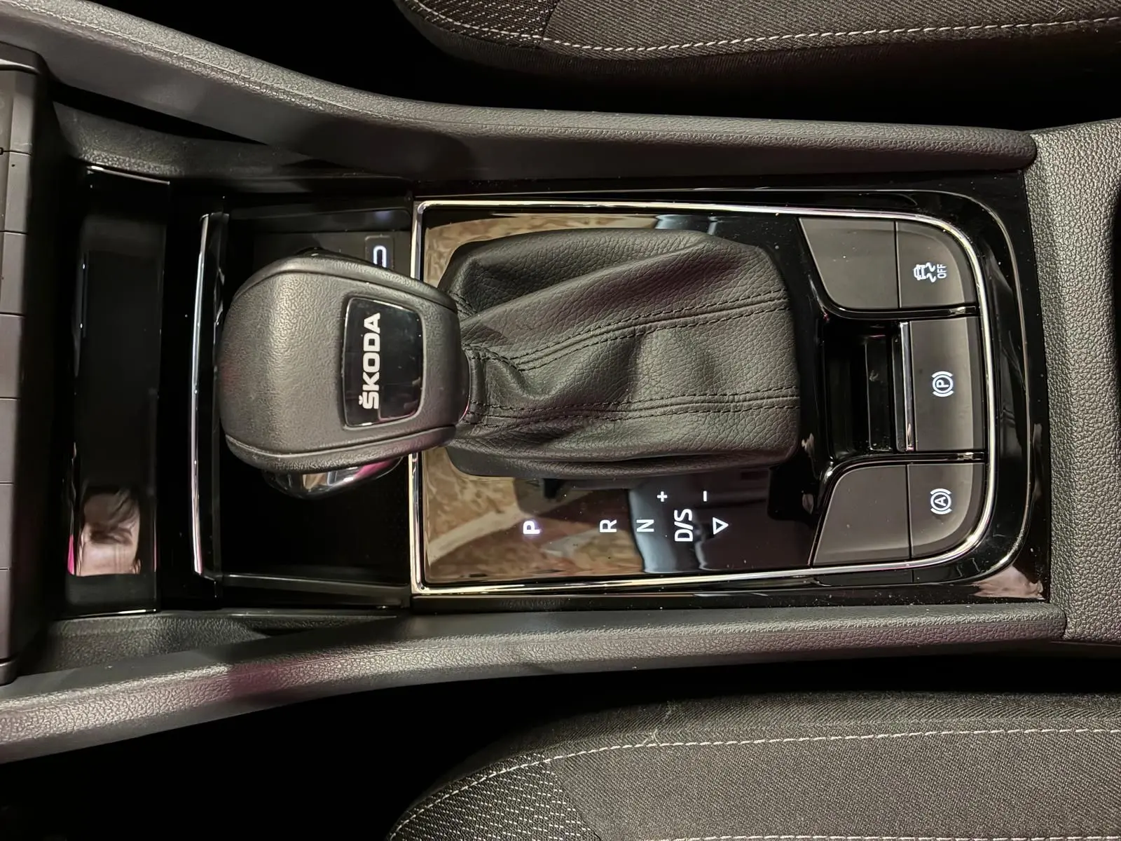 Gros plan sur la console centrale avec levier de vitesse automatique noir marqué SKODA, entouré de boutons de contrôle.