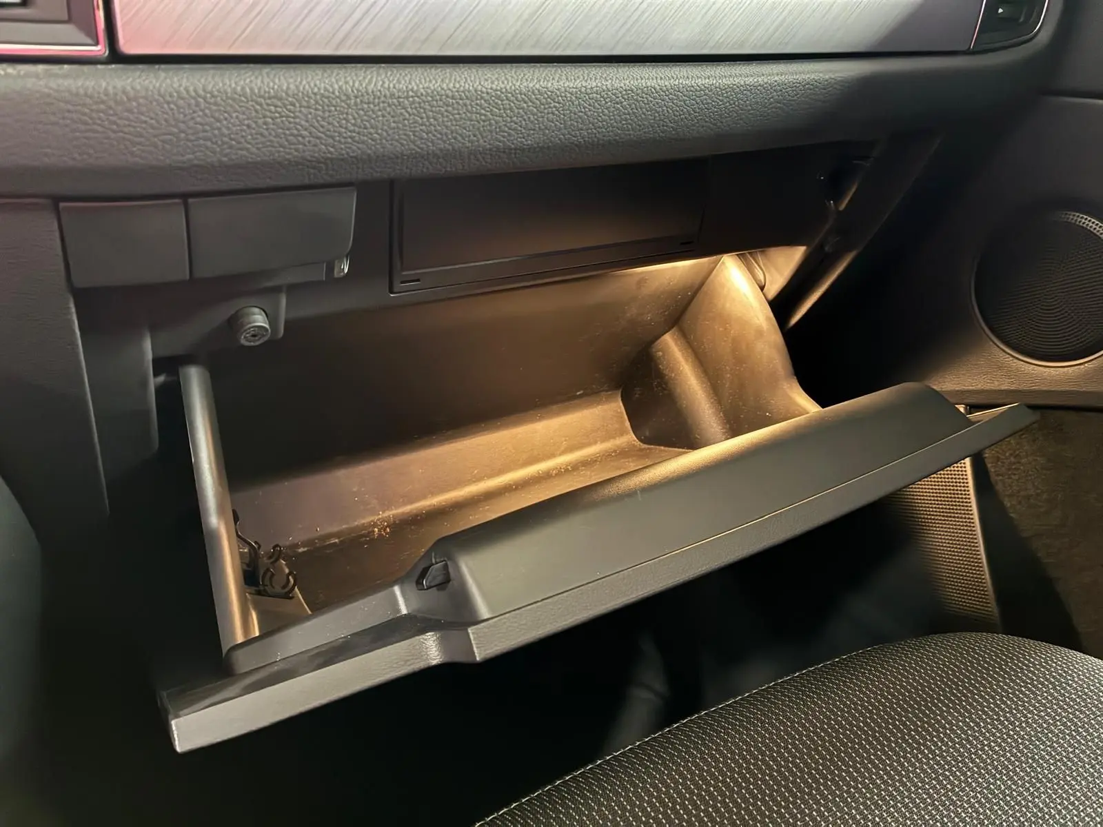 Vue intérieure du coffre à gants ouvert du Skoda Kodiaq gris clair 2023, mettant en valeur l’éclairage intérieur et le tissu noir des sièges.