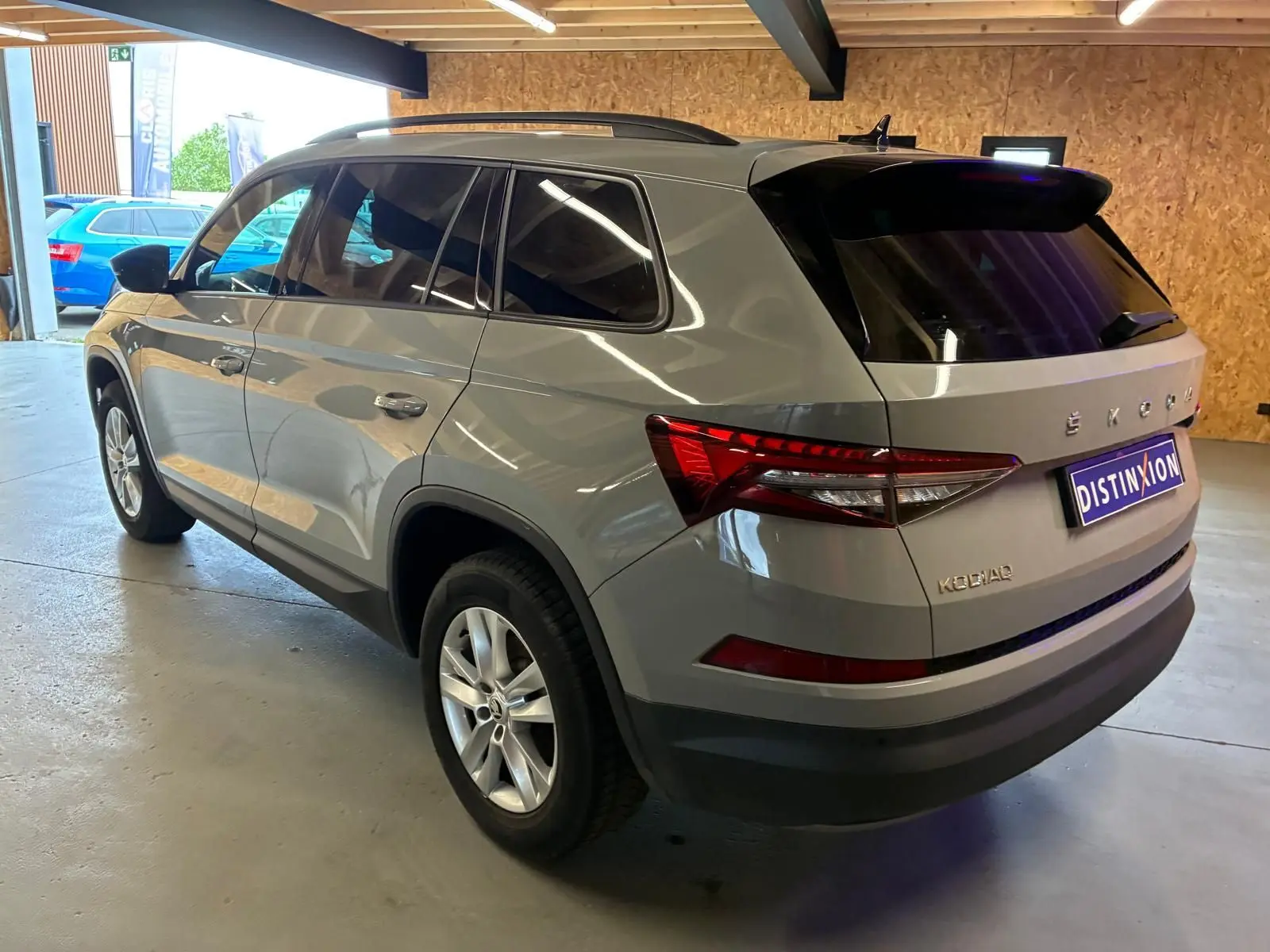 Vue 3/4 arrière droite d'un Skoda Kodiaq gris clair 2023 avec feux arrière LED et vitres teintées en intérieur d'atelier.