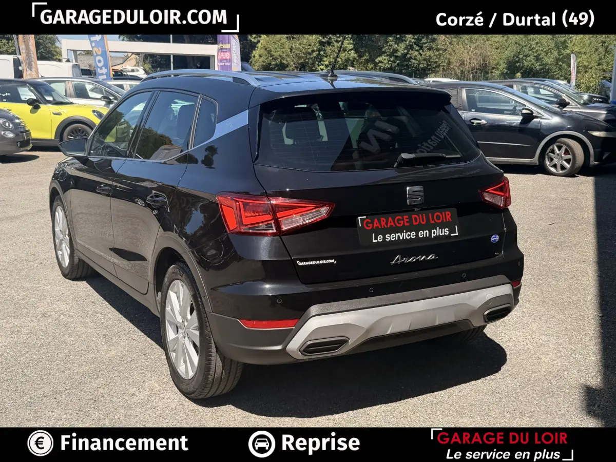 Vue 3/4 arrière droite d'une SEAT Arona noire 2025 avec jantes alliage et barres de toit chromées sur parking.
