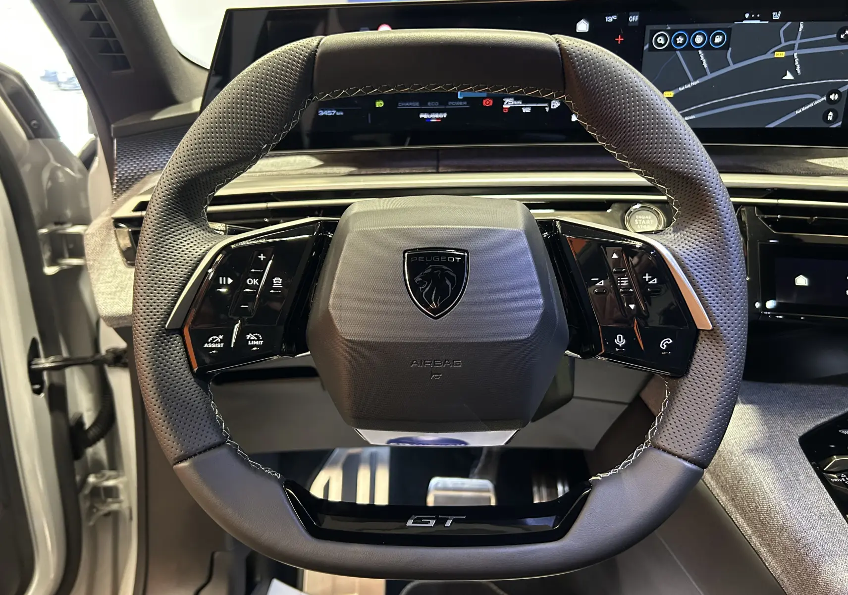 Vue rapprochée du volant GT perforé du Peugeot 3008 Hybrid blanc, avec tableau de bord numérique et commandes intégrées.