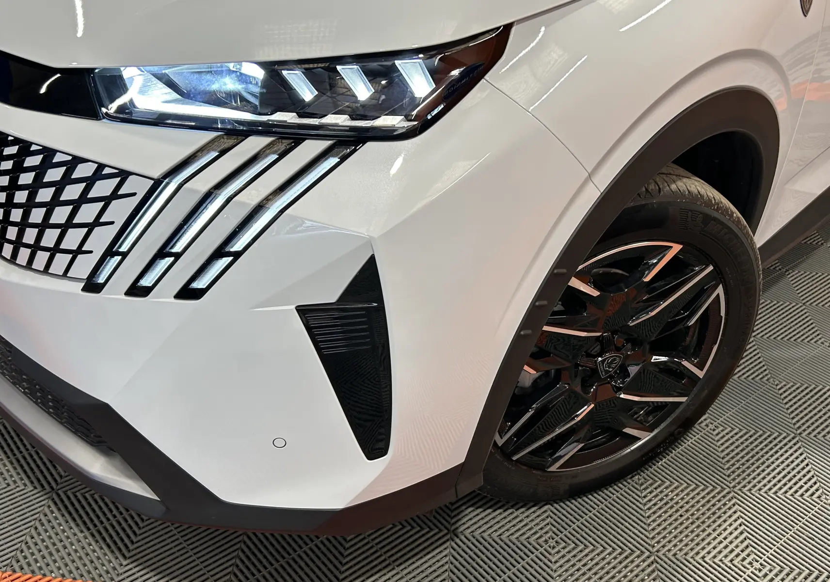 Gros plan sur l’avant droit blanc Okenite du Peugeot 3008 III Hybrid, mettant en valeur les phares LED et la jante noire brillante.