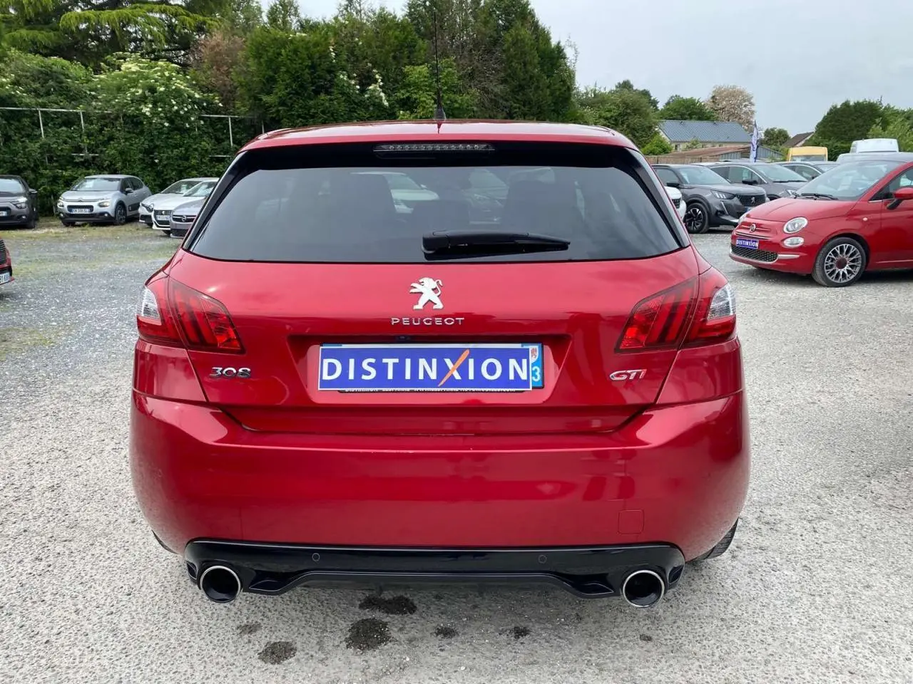 Vue arrière d'une Peugeot 308 GTi rouge métallisée avec double sortie d'échappement et vitre arrière teintée.