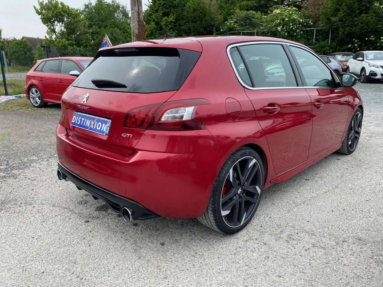Peugeot 308 GTi rouge vue 3/4 arrière droit, avec jantes noires et double sortie d'échappement chromée.