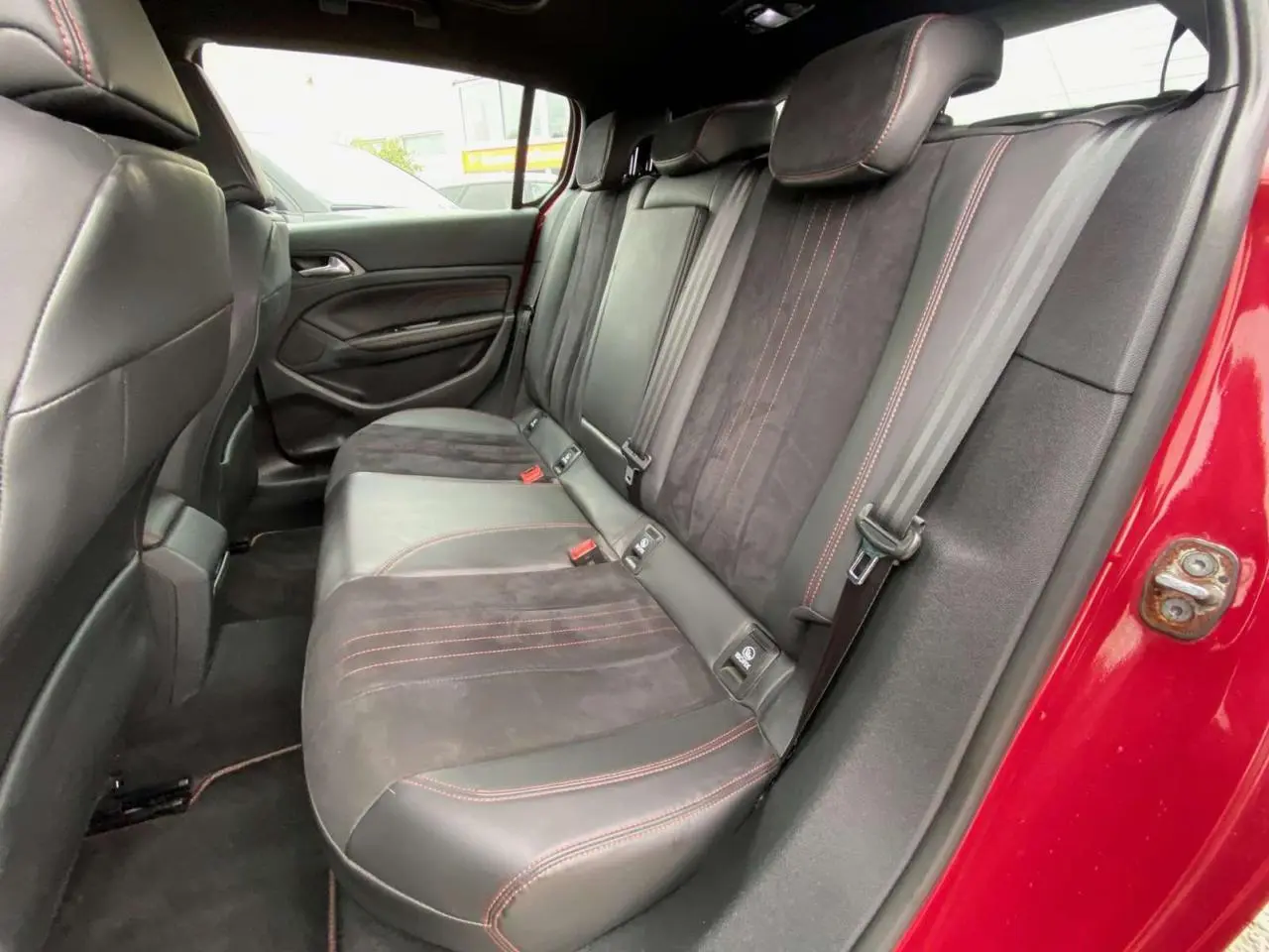 Vue intérieure côté arrière droit de la banquette en cuir noir avec surpiqûres rouges d'une Peugeot 308 GTi rouge.