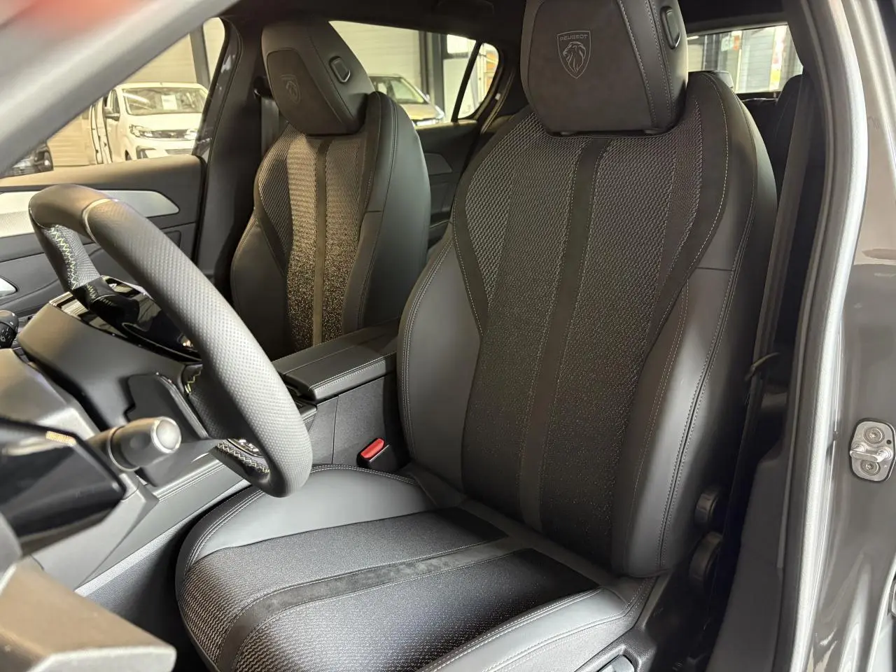 Vue intérieure côté conducteur de la Peugeot 308 gris selenium, sièges en cuir et tissu avec logo Peugeot brodé sur appuie-tête.